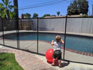 Child looking through Mesh Pool Fence with Beach Ball