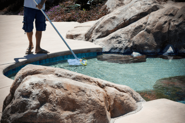 man using a pool net to clean a swimming pool