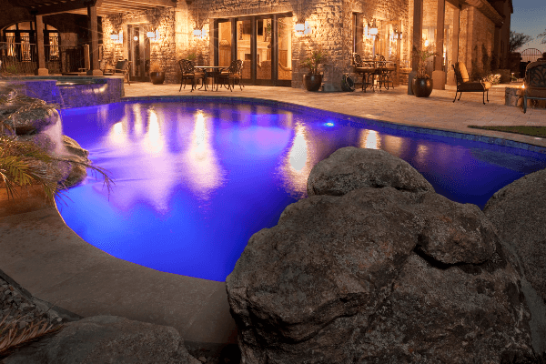 irregular backyard pool with pool lights illuminating the water