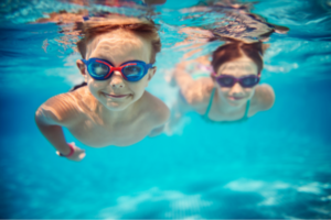 two children swimming in a pool with goggles on