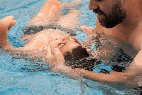 man holding the head of a child while in a pool during aquatic therapy