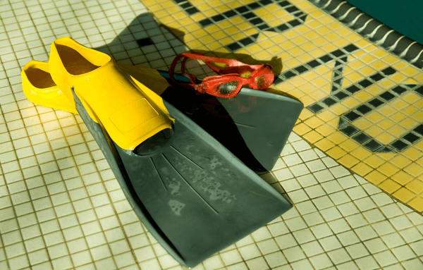 swim fins and goggles beside the edge of a pool