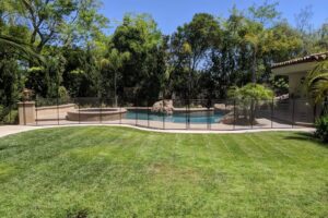 Beautiful backyard swimming area with a black mesh pool fence installed