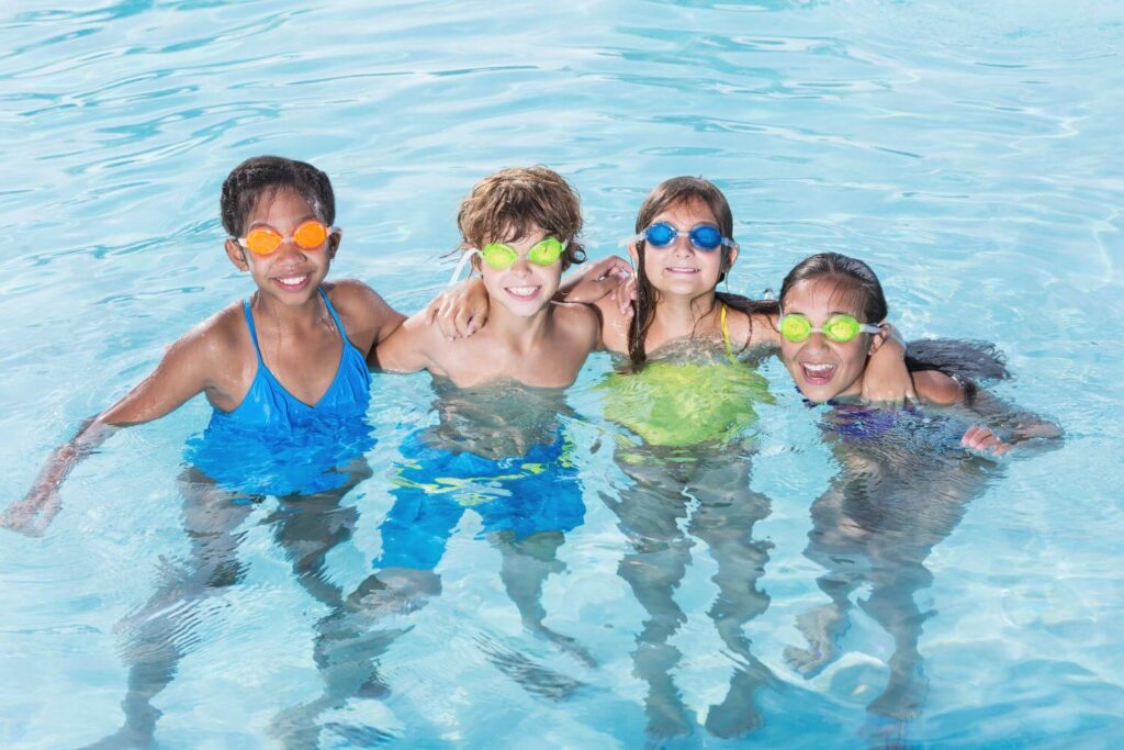 four young friends wearing goggles are locking arms in a swimming pool