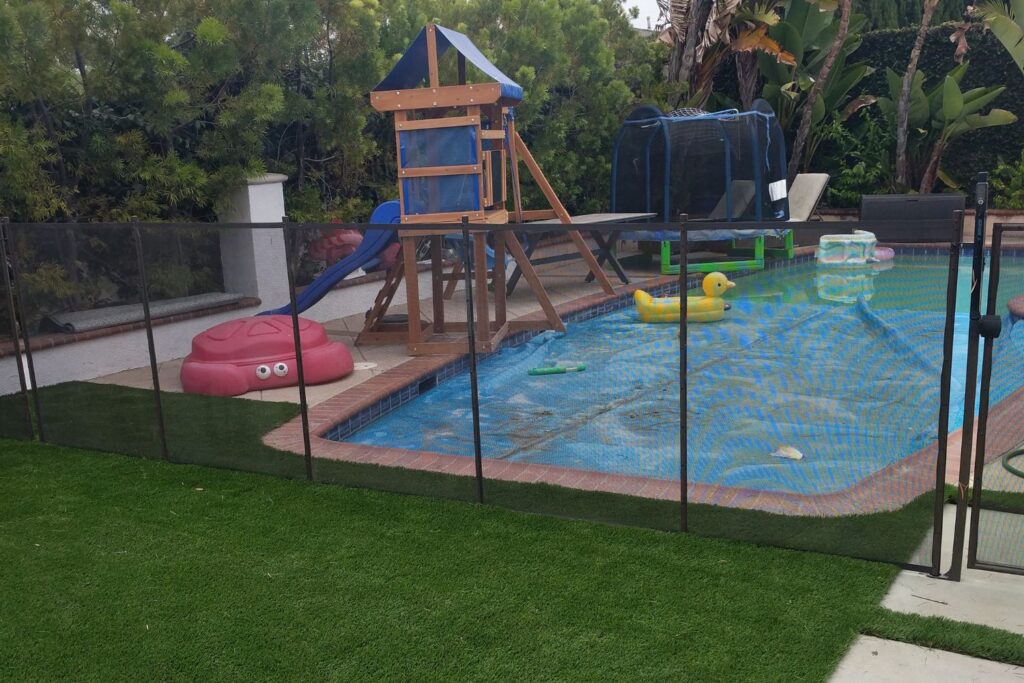 Pool with play structure and trampoline surrounded by a black mesh pool fence