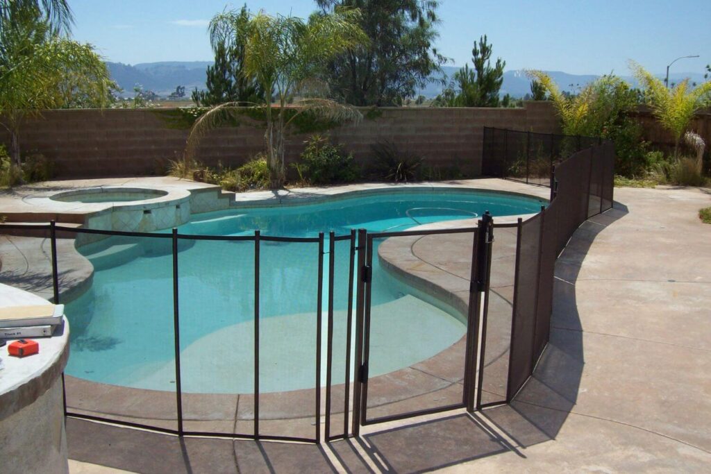 Black mesh removable pool fence installed around an irregular shaped swimming pool
