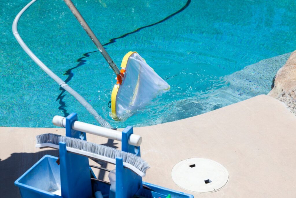 Pool cleaning net and brush next to a swimming pool