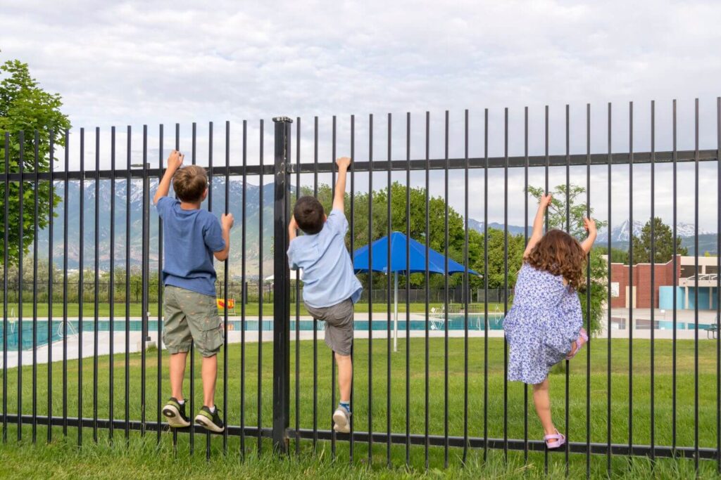 Three young children trying to climb a metal fence around a pool