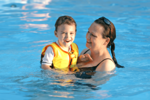 woman in swimming pool holding a boy in a yellow vest