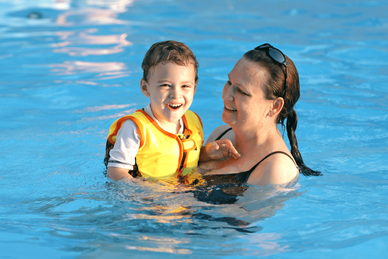 woman in swimming pool holding a boy in a yellow vest