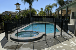 Backyard pool and hot tub surrounded by a black mesh pool fence.