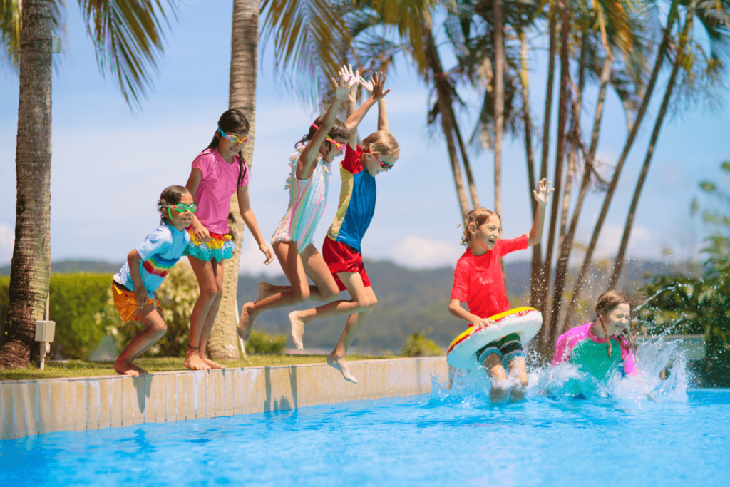 A group of children playing around and jumping into a pool