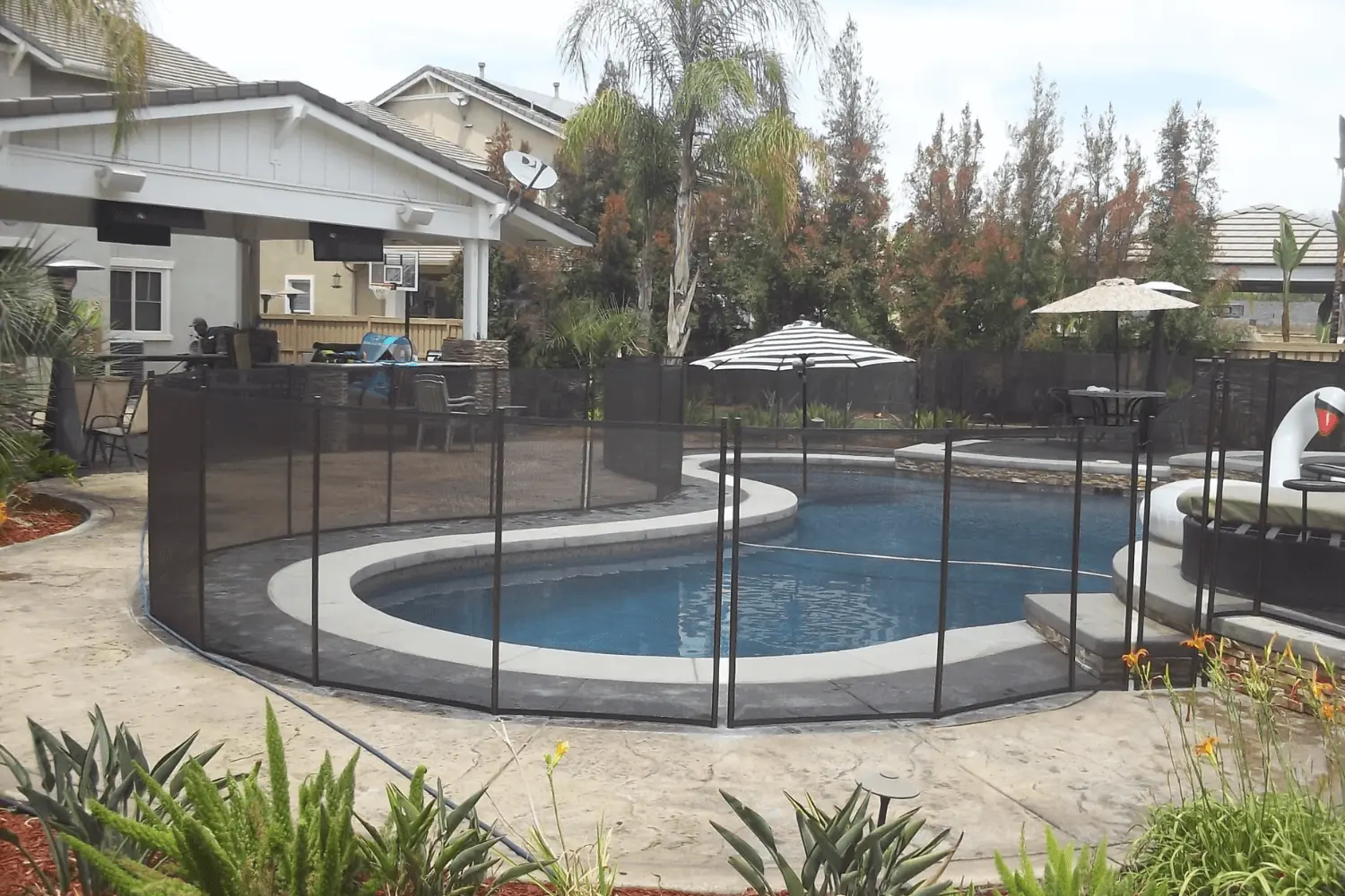 Swimming pool in a back yard with a mesh safety fence around it