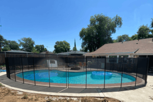 Backyard swimming pool with black mesh pool fence surrounding it and solar sun rings floating in the water