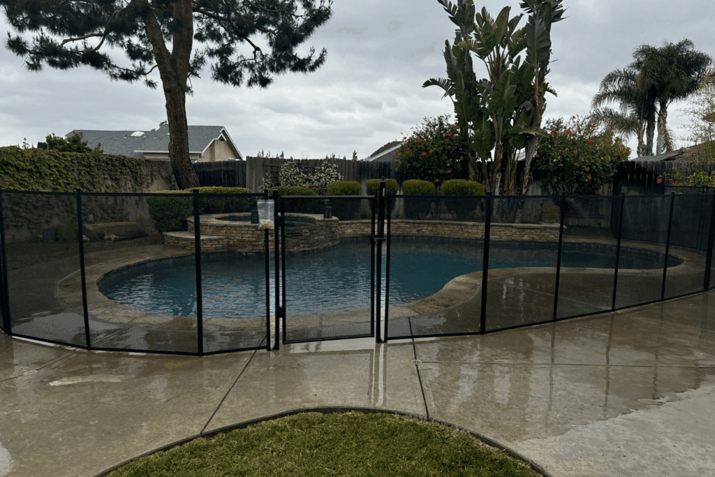 Photo of a backyard swimming pool surrounded by removable mesh pool fence on a stormy day