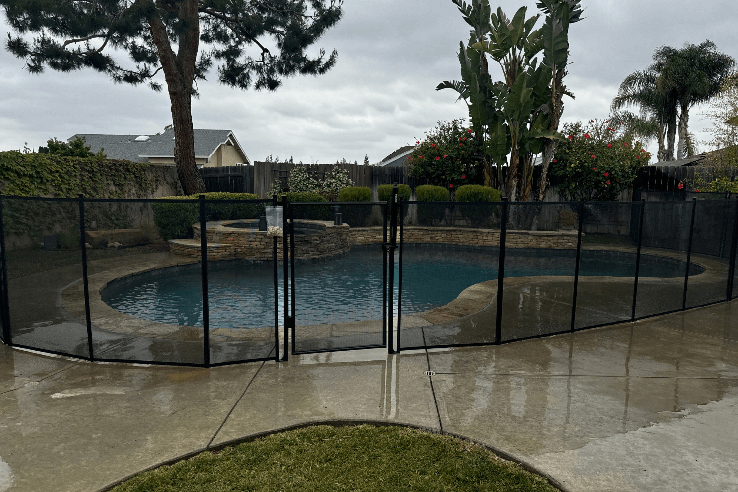 Photo of a backyard swimming pool surrounded by removable mesh pool fence on a stormy day