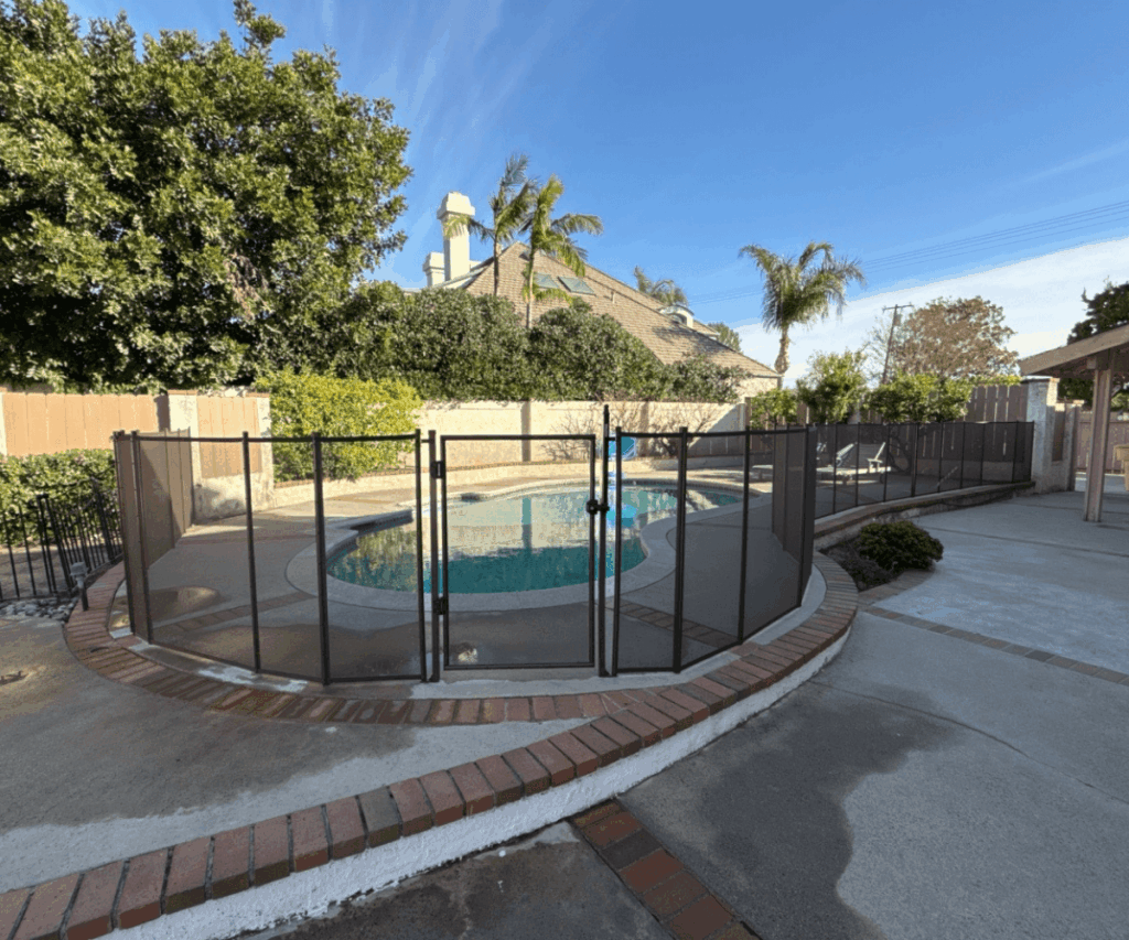 black mesh pool fence newly installed around a large irregular shaped swimming pool