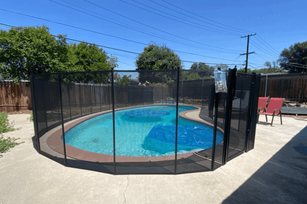 black mesh removable pool fence installed around a swimming pool with solar blankets floating on the water