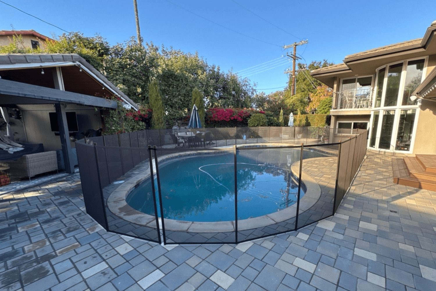 brown mesh removable pool fence installed on pavers in a backyard