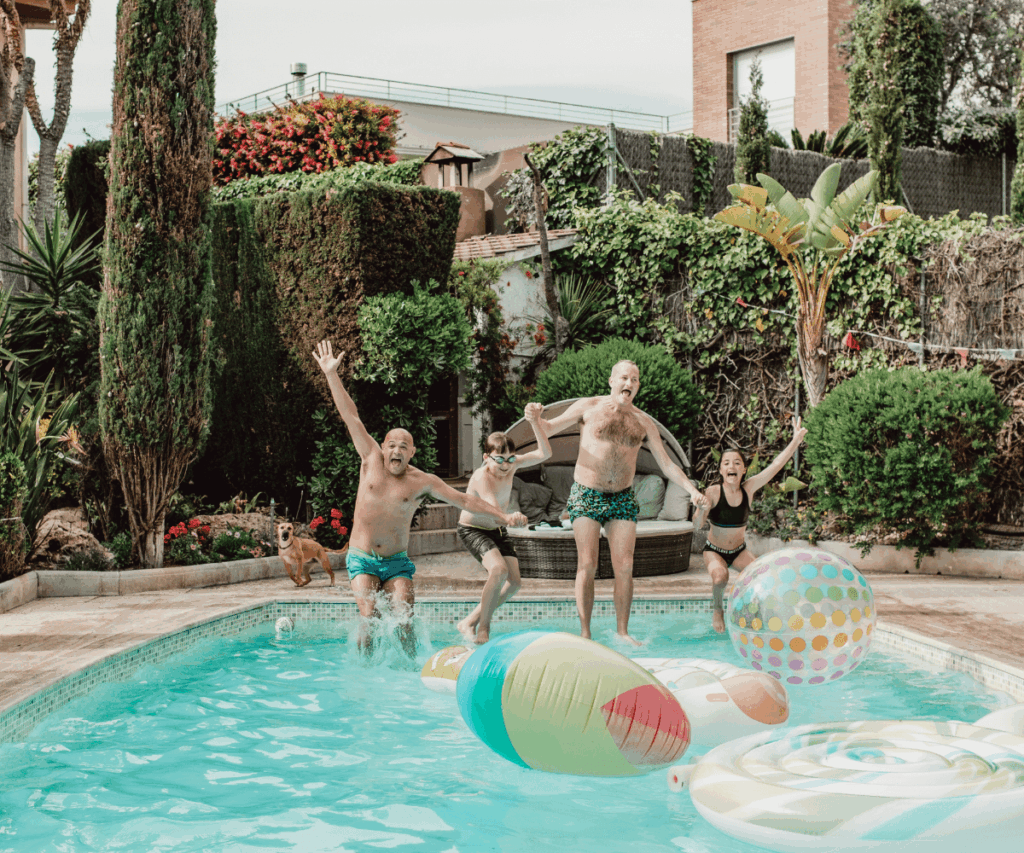 family holding hands while jumping into a swimming pool as their dog watches on from the deck