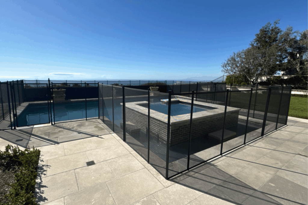A backyard pool that is enclosed on all sides by a black mesh safety fence