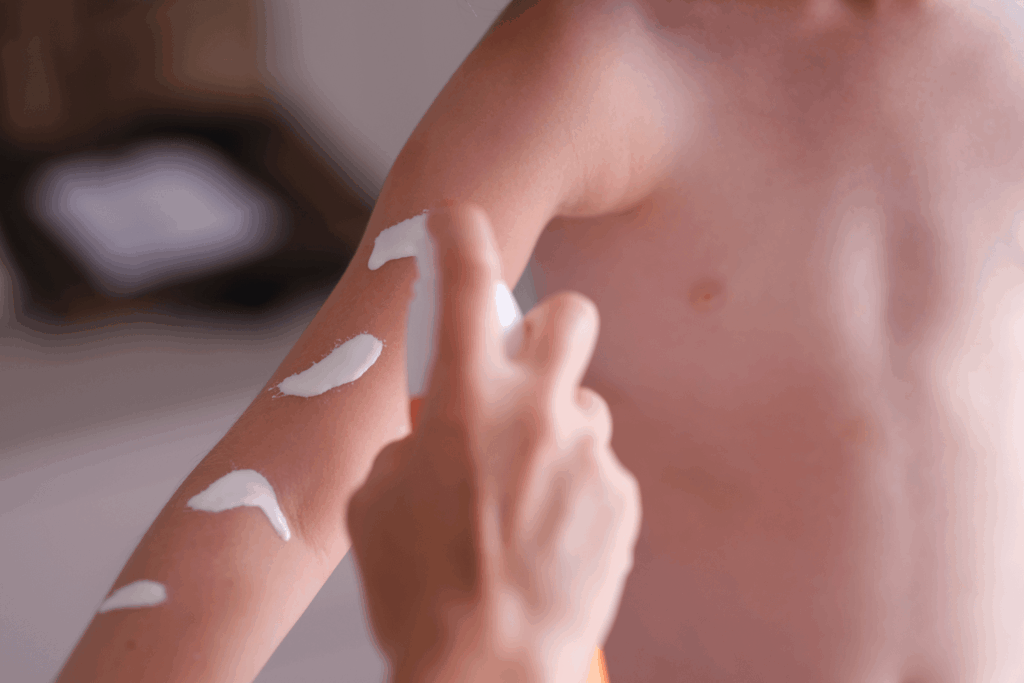 an adult hand pumping white sunscreen onto a child's arm
