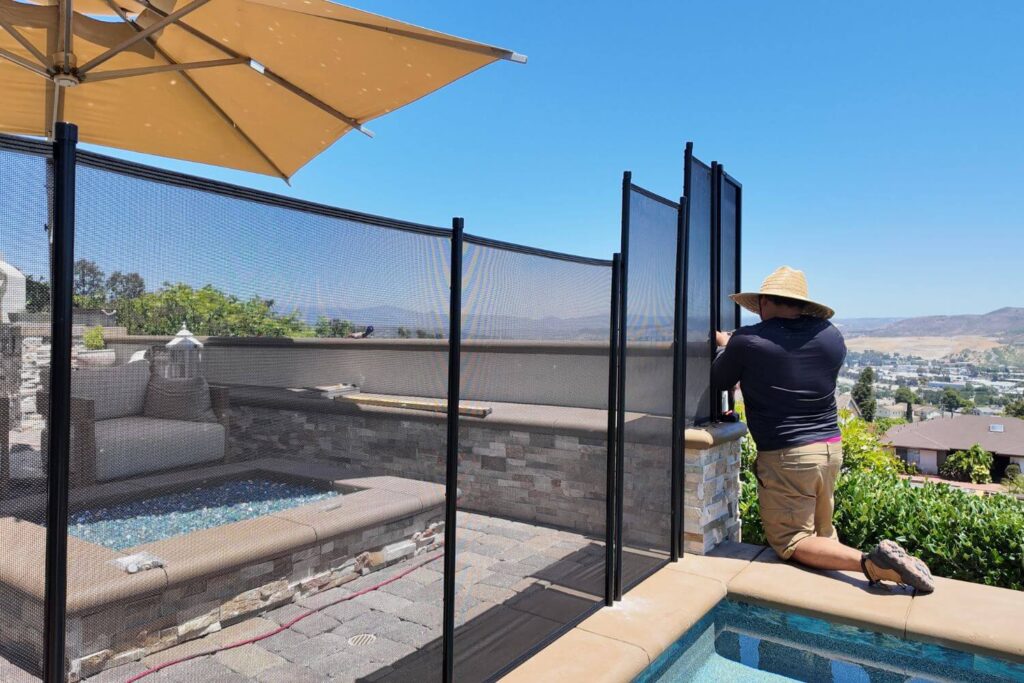 Man kneeling down as he repairs a mesh pool fence installed around a swimming pool