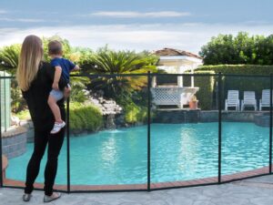 Mother holding her toddler while they stand in front of an installed mesh pool fence around the swimming pool