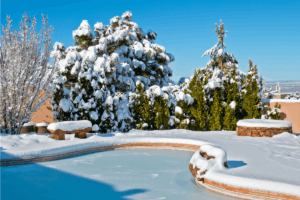 A backyard swimming pool and deck covered in snow after a snowstorm