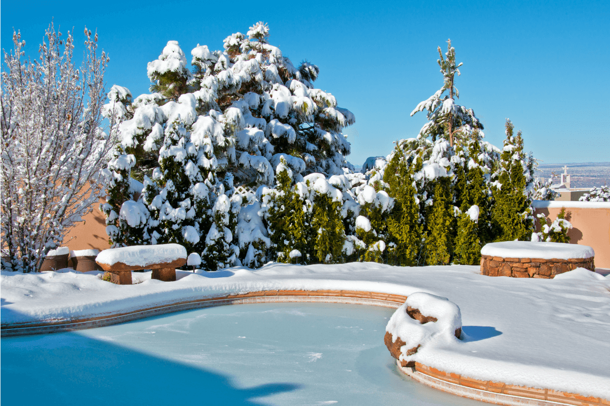 A backyard swimming pool and deck covered in snow after a snowstorm
