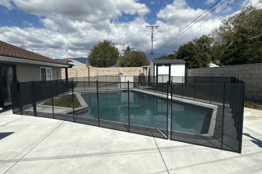 Backyard swimming pool with a black mesh removable pool fence installed surrounding it
