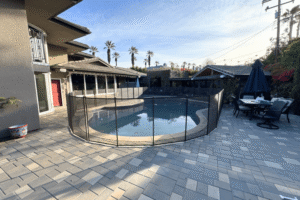 Large backyard patio and swimming pool surrounded by a black mesh removable pool fence