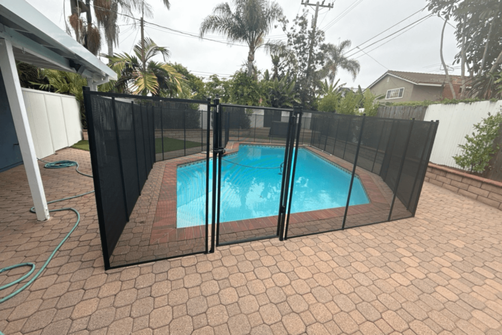 A Backyard patio area with an in-ground pool area with a black mesh fence around the pool's perimeter.