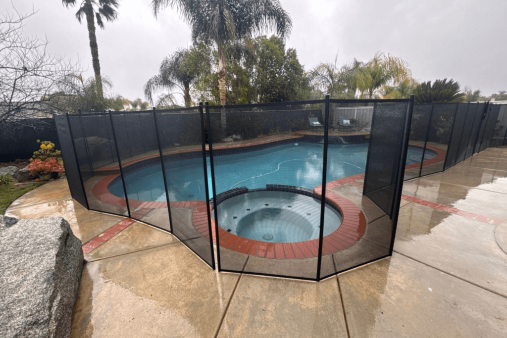 Backyard pool and in-ground hot tub with a black mesh safety fence around it.
