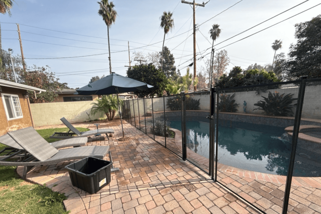A backyard pool with a paver deck and black mesh safety fence around it.
