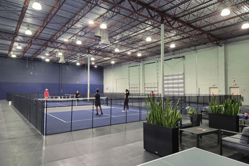 A group of people playing a game of pickleball on an indoor court surrounded by black mesh removable pool fencing by All-Safe