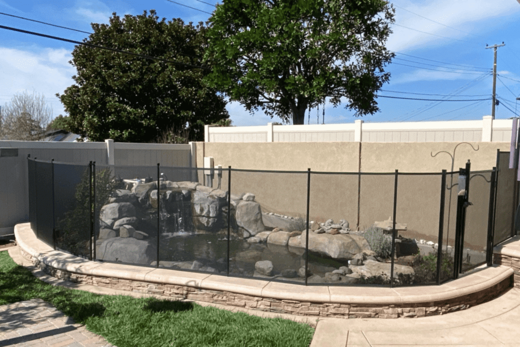 A small backyard pool with a rock waterfall surrounded by a mesh safety fence.