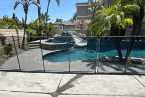 A concrete pool deck with palm tree landscaping and a mesh safety fence installed.