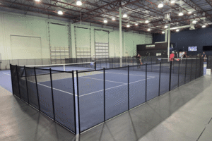 Black mesh removable pool fencing installed surrounding an indoor pickleball court