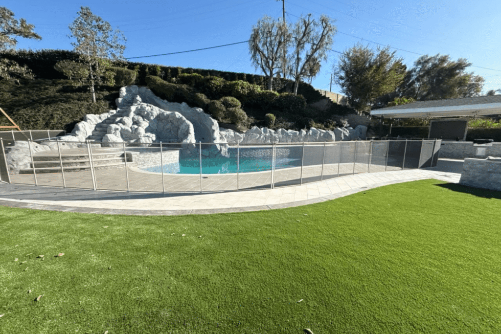 A backyard pool with a large rock water slide feature and pool safety fence around it.
