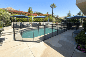 black mesh pool fence installed around a swimming pool with three blue umbrellas