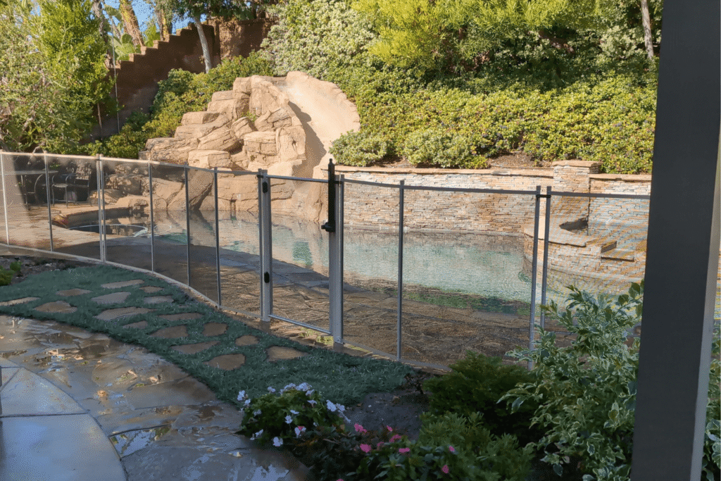 tan pool fence installed around a swimming pool with a rock feature and slide