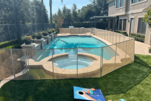 tan mesh pool fence installed around a swimming pool and hot tub