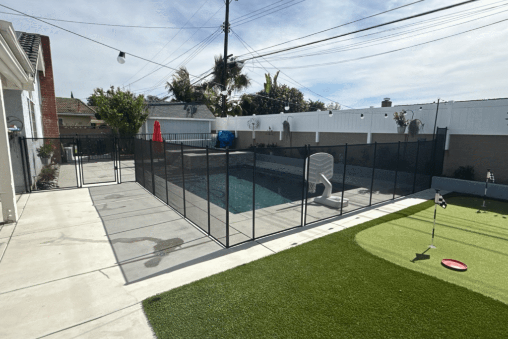 swimming pool enclosed by a pool fence next to a putting green in a backyard