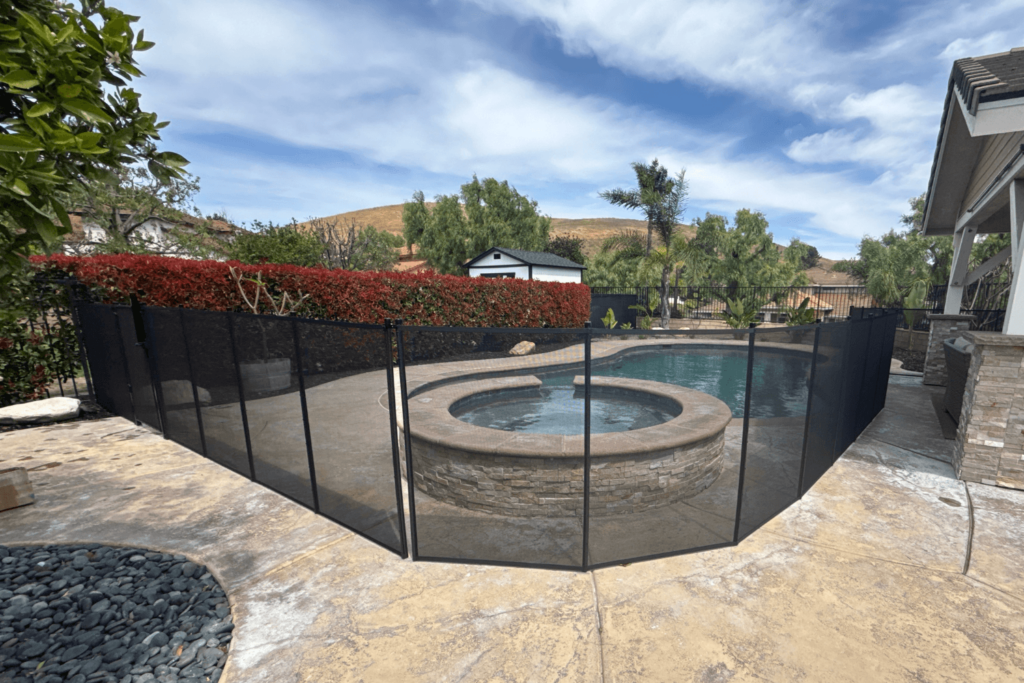 Black mesh removable pool fence installed around a swimming pool. Area around the fence is kept clear from obstacles