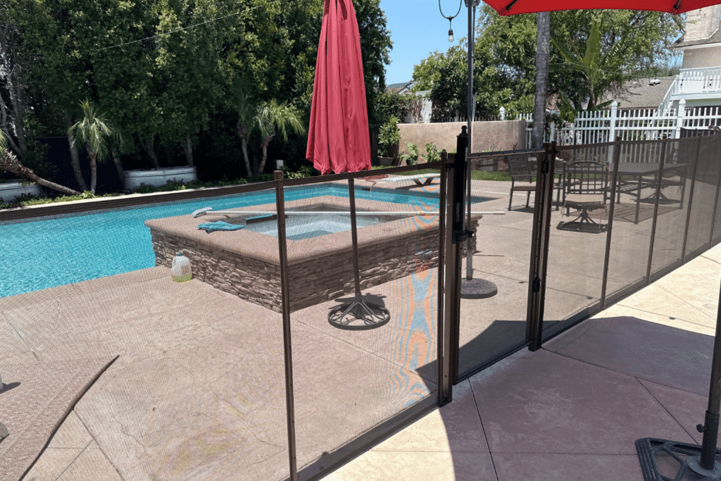 swimming pool enclosed by a black mesh pool fence and a safety gate that opens towards the house