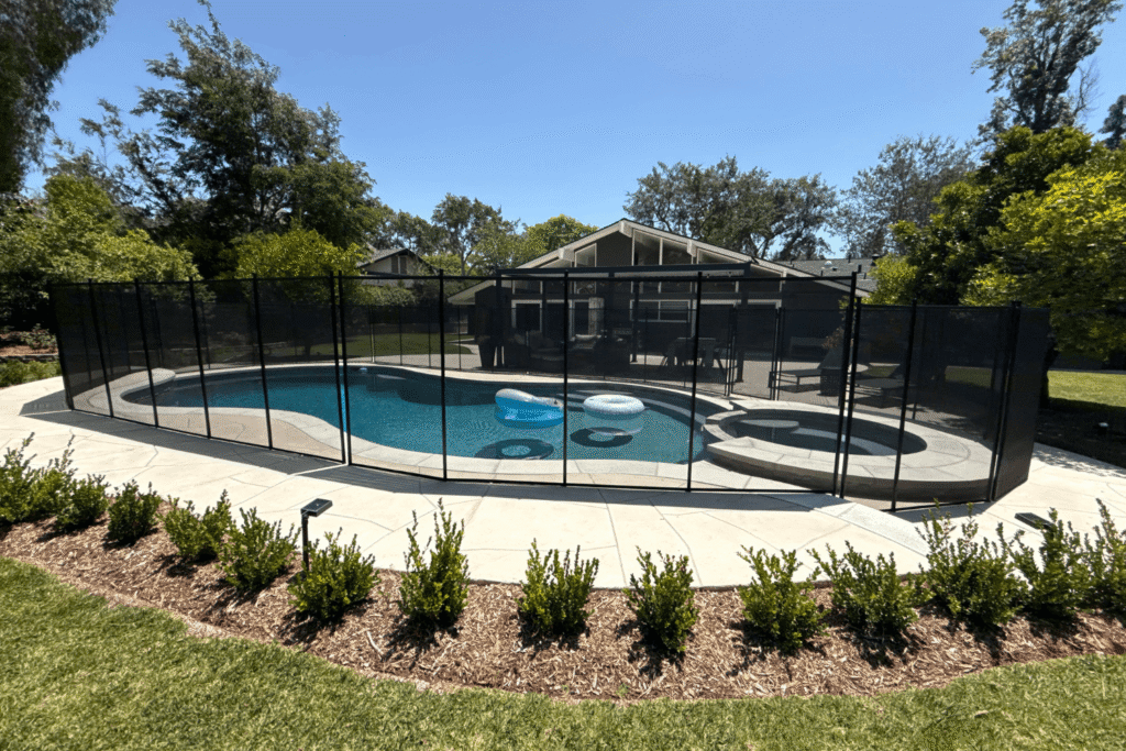 black mesh pool fence surrounding a swimming pool with beautiful landscaping around it