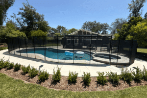 black mesh pool fence surrounding a swimming pool with beautiful landscaping around it