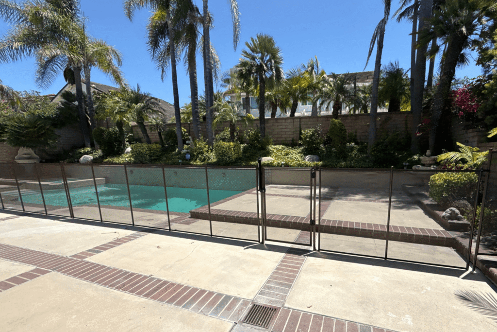 brown mesh pool safety fence bordering a backyard swimming pool