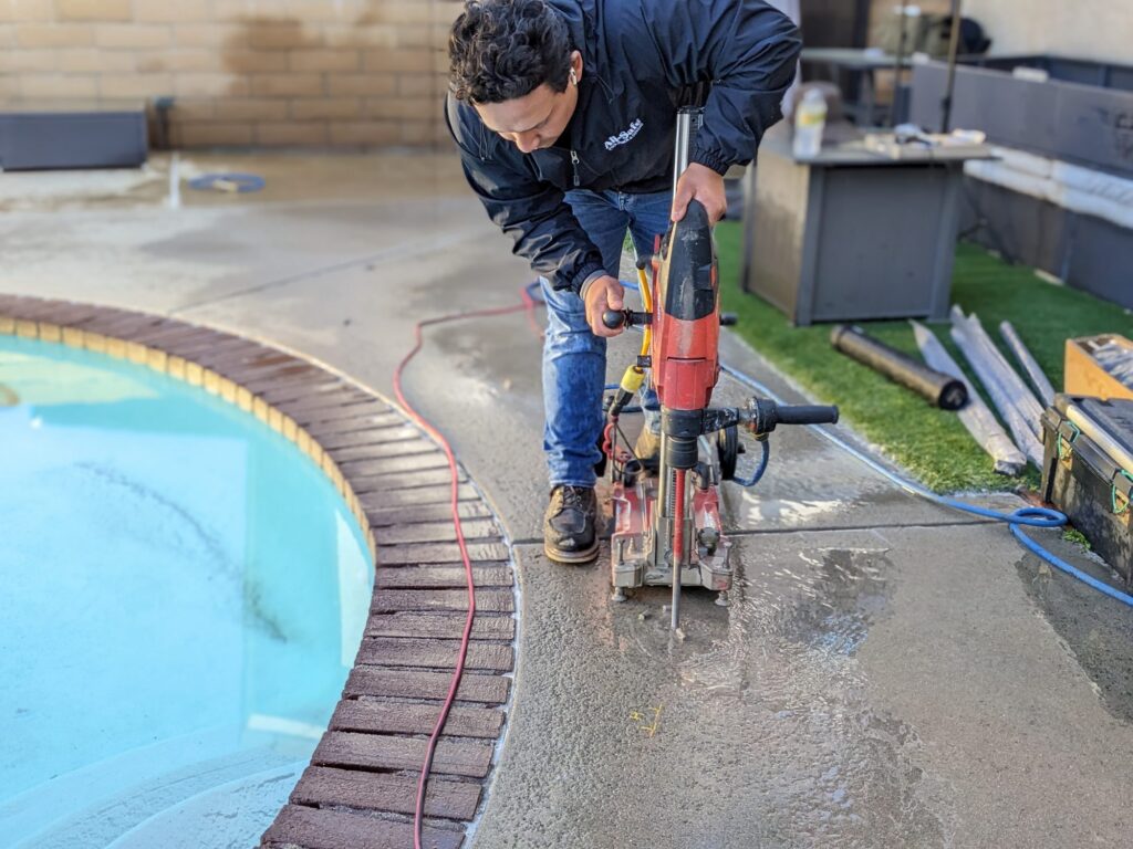Pool fence installer core drilling a hole in a concrete pool deck for a removable mesh fence